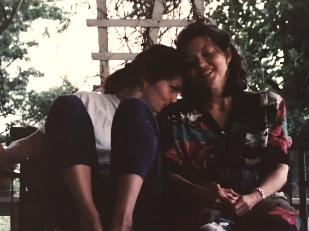 Vintage photo of a young woman leaning into an older woman who is laughing warmly, seated together outdoors