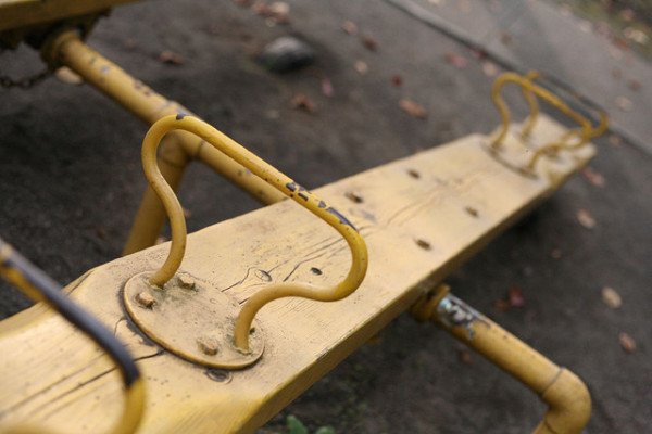 Close-up of a weathered yellow seesaw on a playground, showing worn paint and metal handles