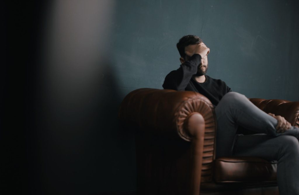 Man sitting alone in a leather armchair with his hand covering his face, appearing emotionally overwhelmed or distressed